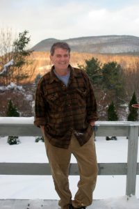 Man standing against a fence against a nature background.